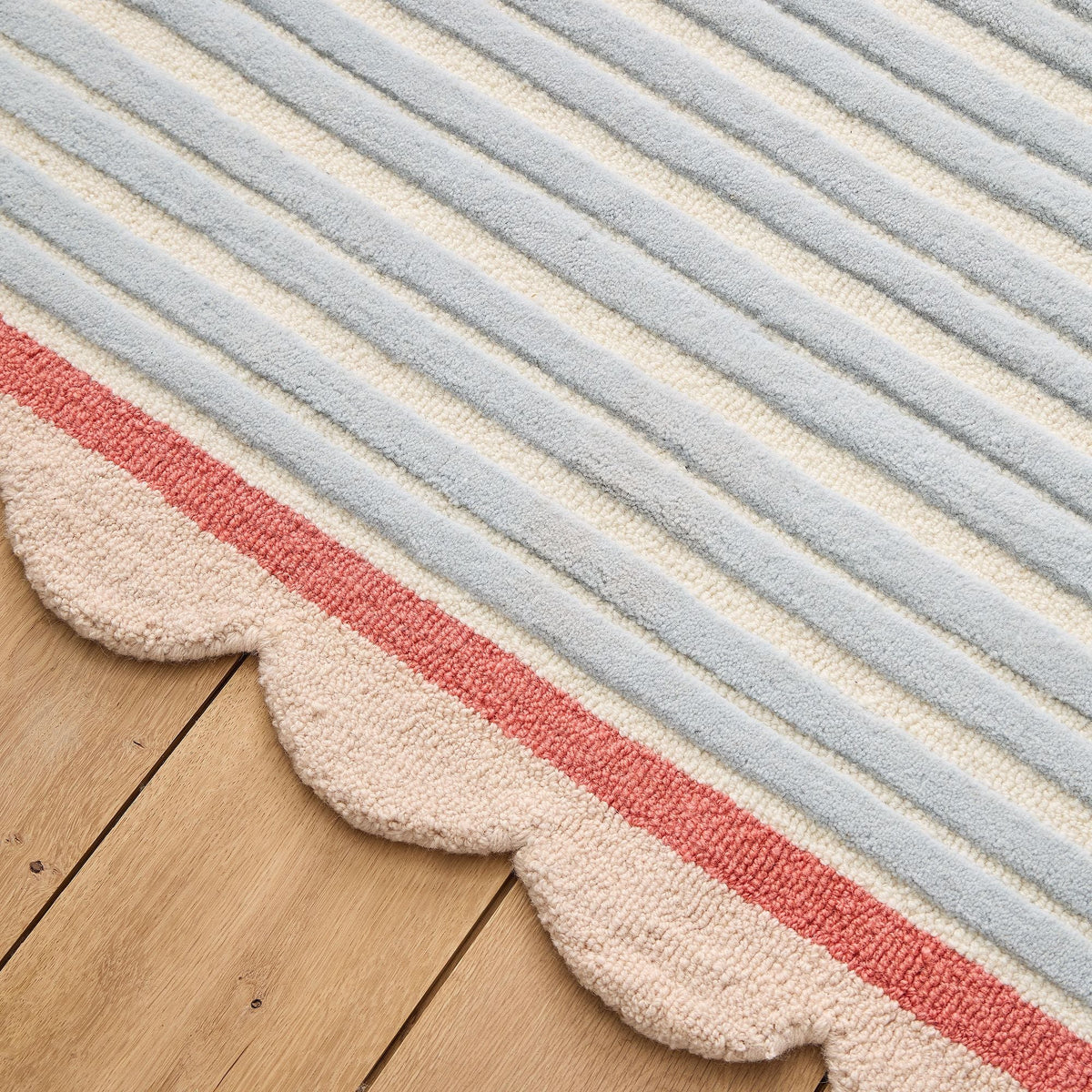 Pastel blue striped wool area rug with a scalloped beige border styled in a bright modern living room with neutral decor.