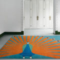 Hand tufted wool peacock rug by COZY CARPETS featuring vibrant orange fan-shaped feathers, turquoise accents, and a royal blue peacock design in an elegant modern entryway.