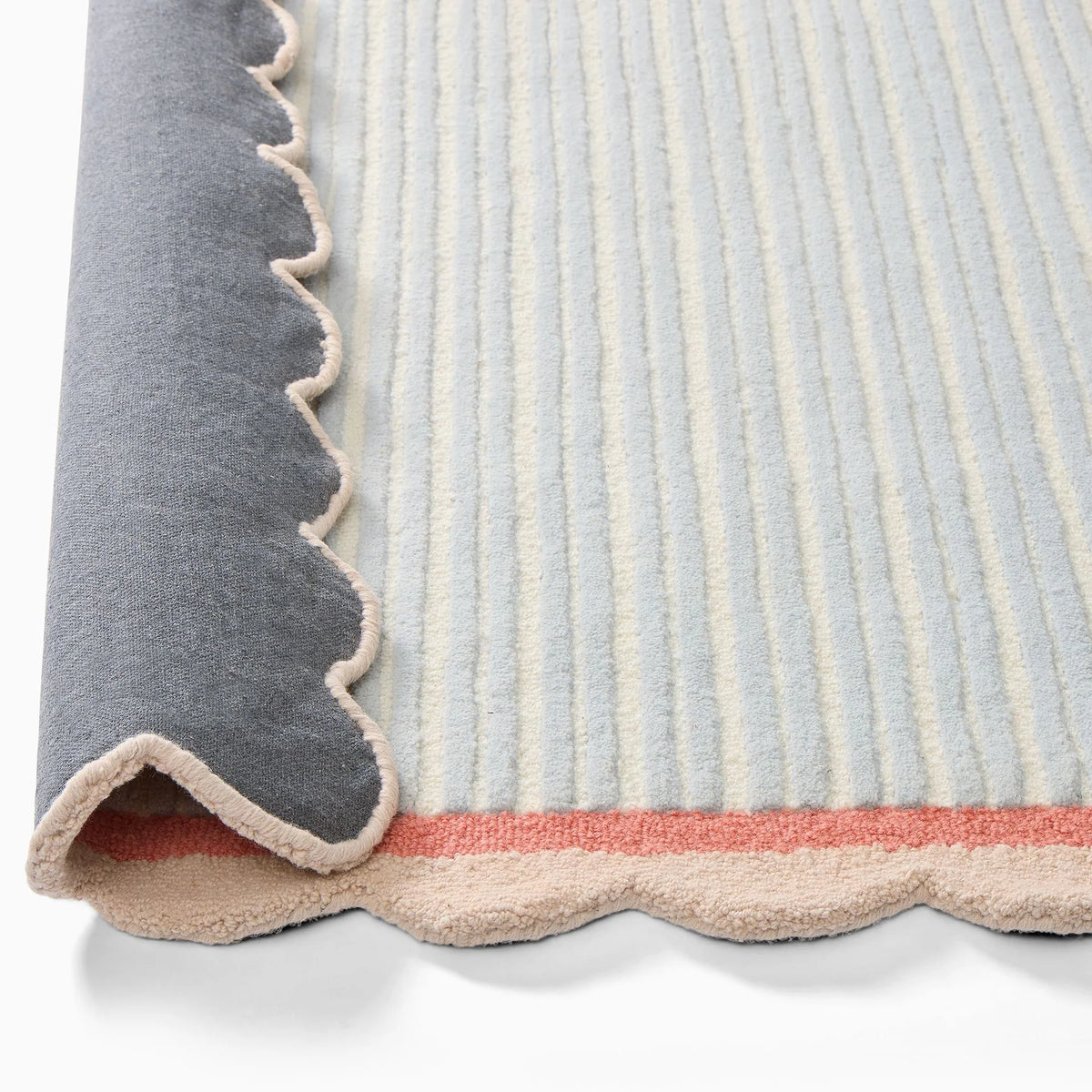 Close-up of the scalloped beige edge and coral pink border on a pastel blue and ivory hand-tufted wool rug from COZY CARPETS.