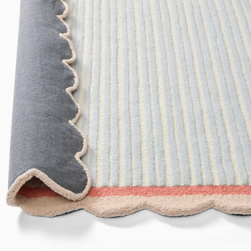 Close-up of the scalloped beige edge and coral pink border on a pastel blue and ivory hand-tufted wool rug from COZY CARPETS.