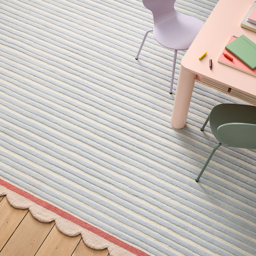 Top view of a rectangular hand-tufted wool rug with pastel blue and ivory stripes, coral trim, and a decorative scalloped beige outline by COZY CARPETS.